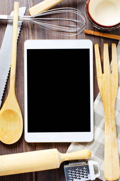 A tablet computer and cooking battery on a brown wooden background. Copy space. Concept of cooking recipes A tablet computer and cooking battery on a brown wooden background. Copy space. Concept of cooking recipes. confectioner photos stock pictures, royalty-free photos & images