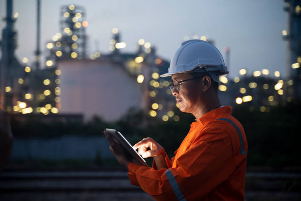 engenheiro usando tablet perto da refinaria de petróleo à noite. - fuel and power generation oil industry petroleum industry - fotografias e filmes do acervo