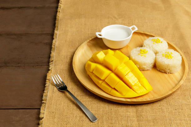 istock Yellow half  mango with small fork. Mango fruit cubes on the wooden table. Tropical fruit asia. Fresh yellow mango peel and Sliced cubes on wood butcher. Dessert fruit. 1250283158