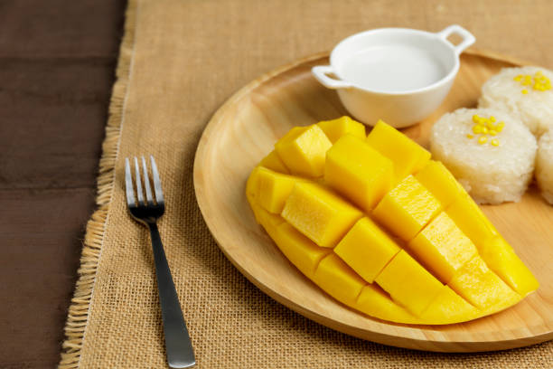 istock Close up Yellow half  mango with small fork. Mango fruit cubes on the wooden table. Tropical fruit asia. Fresh yellow mango peel and Sliced cubes on wood butcher. Dessert fruit. 1250283297
