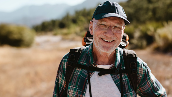 Portrait of a senior man carrying a backpack looking at camera and smiling. Fit old man on a hiking trip.