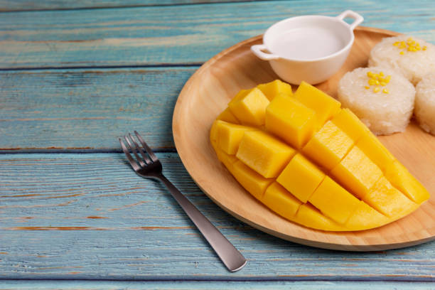 istock Yellow half  mango with small fork. Mango fruit cubes on the Blue wooden table. Tropical fruit asia. Fresh yellow mango peel and Sliced cubes on wood butcher. Dessert fruit. Tropical fruit summer concept. 1250290546