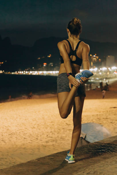 femme brésilienne s’étirant après le jogging au point de vue de bord de mer de plage d’ipanema la nuit - shorts rear view summer beach photos et images de collection