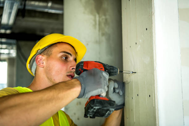 istock Young male construction worker in yellow hardhat drilling the wall with electric drill tool. Close-up front portrait with copy space 1250290727
