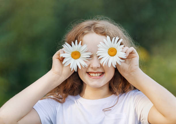 Child with daisy eyes showing white healthy  teeth  on green background in a summer park.
