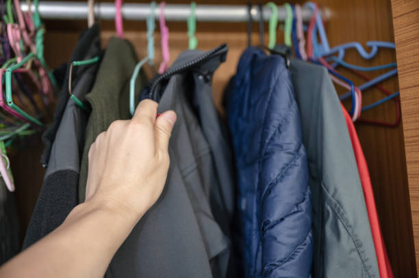 Hand choosing winter jacket on clothes rack in closet
