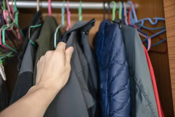Hand choosing winter jacket on clothes rack in wood closet