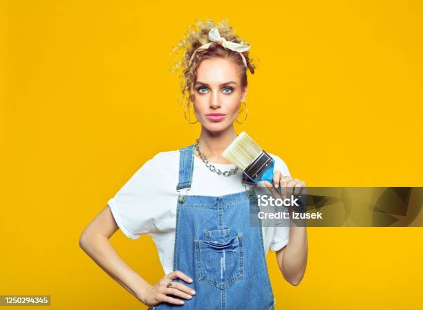 Young Woman In Coveralls Holding Paintbrush Stock Photo - Download Image Now - House Painter, Colored Background, Authority