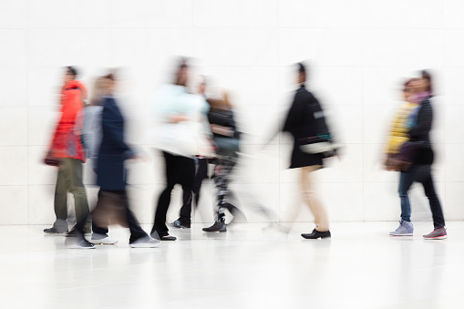 Large group of motion blurred people walking in modern hallway, London