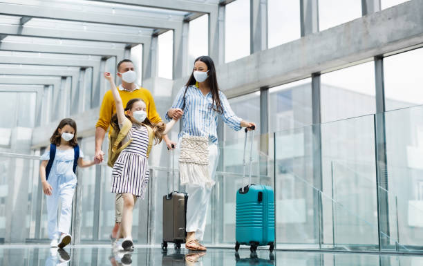 familia con dos hijos que se van de vacaciones, con máscaras faciales en el aeropuerto. - coronavirus fotos fotografías e imágenes de stock