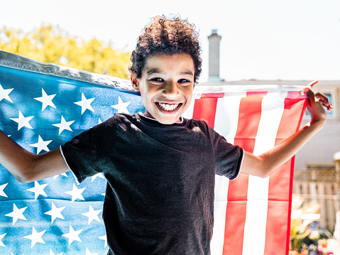 Black boy holding American National flag while standing on a diving board by the backyard pool.