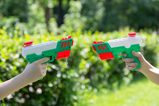 Kids hands with water guns. Children play with water guns in the park or garden on bright sunshine summer day.