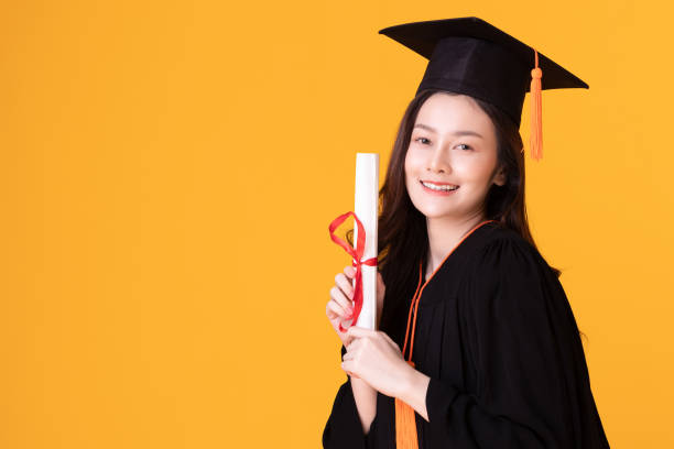 счастливый выпускник азиатской женщины в кепке и гоум проведения сертифицированный или диплом на желтом фоне,летний выпускной концепции - certificated стоковые фото и изображения
