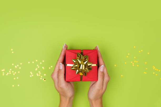 istock Women hands holding a gift or gift box decorated with confetti on a green table top view. 1250306220