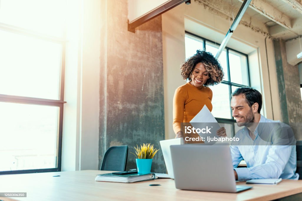 They're staying ahead of the game with their ideas We already have great results! Young beautiful woman working, discussing something with her coworker while standing at office. Business Stock Photo