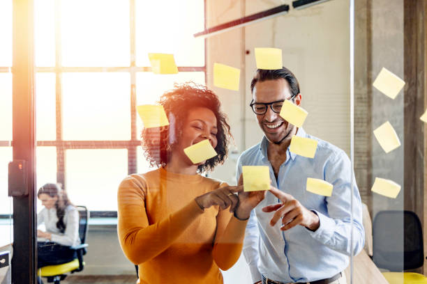 compañeros de trabajo sonrientes escribiendo tareas en papeles pegajosos, publicar notas - planning adhesive note business office fotografías e imágenes de stock