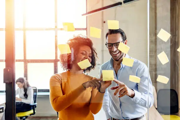 Photo of Smiling coworkers writing tasks on sticky papers, post it notes
