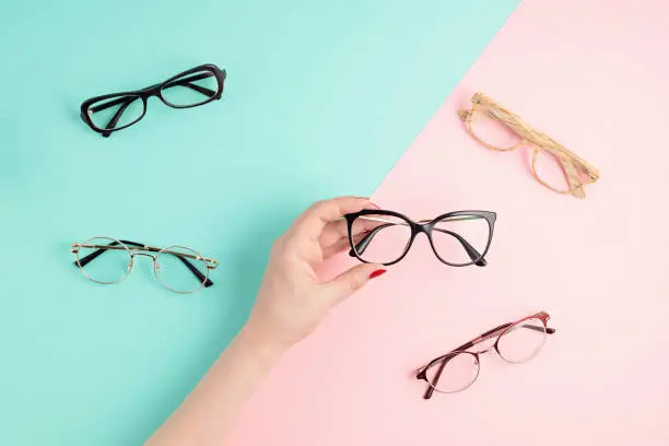 Photo of Woman hand holding eyeglasses. Optical store, glasses selection, eye test, vision examination at optician, fashion accessories concept. Top view