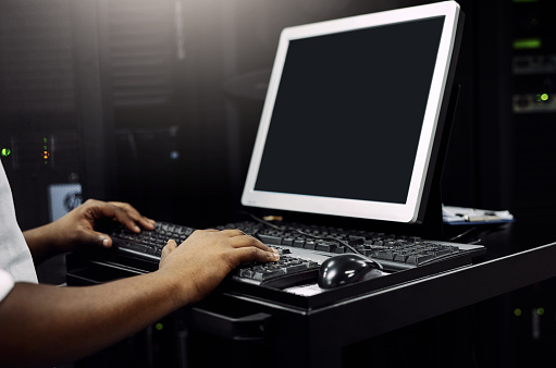 Cropped shot of an unrecognizable IT technician using a computer while working in a data center