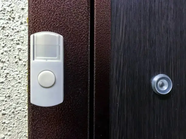 White doorbell or buzzer button on door next to peephole. Entrance door to apartment