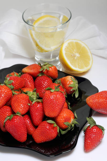 A plate of strawberries and a glass of water with lemon A plate of strawberries and a glass of water with lemon on a light background dissert stock pictures, royalty-free photos & images