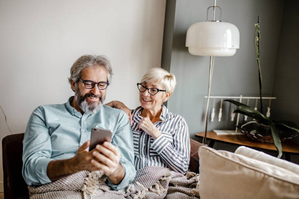 Seniors at home using smart phone Senior couple sitting in a living room at home and woman is holding smart phone old-phone stock pictures, royalty-free photos & images