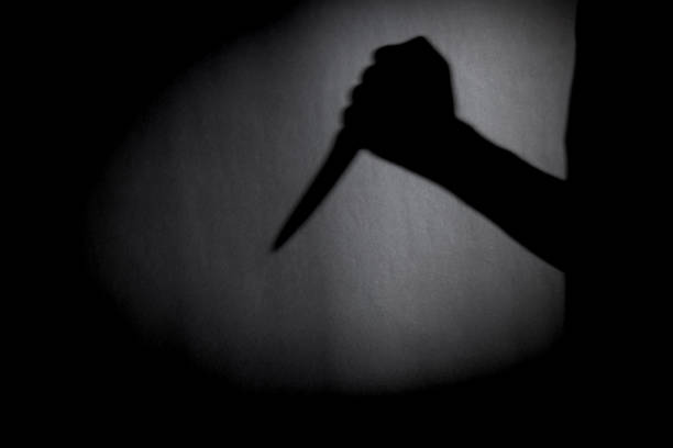 man with knife silhouette over dark wall. black and white photo can be used for illustrating horror and violence attack. crime concept. simple. selective focus. blurred. stock photo