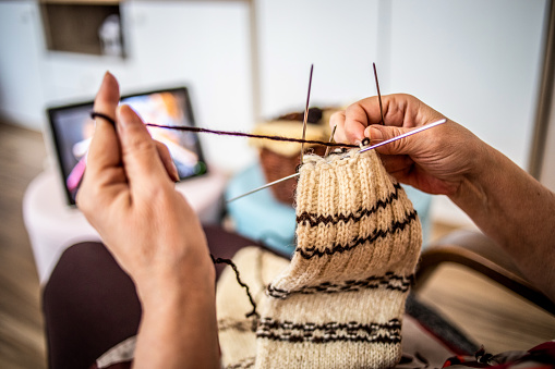 An elderly woman, a pensioner, knits wool socks. An active older woman pursues her hobby
