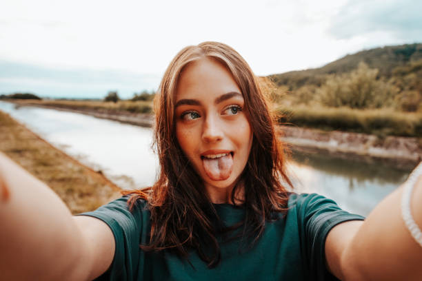 sticking out zunge junge frau, die selfies im freien - mischief people making a face teenage girls stock-fotos und bilder