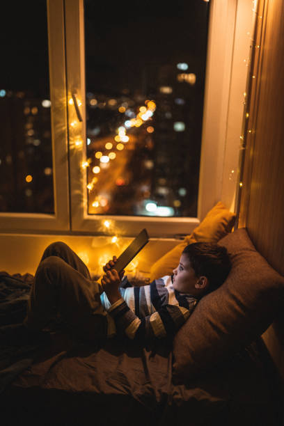 istock Cute little boy lying on bed and reading book on tablet 1250336603