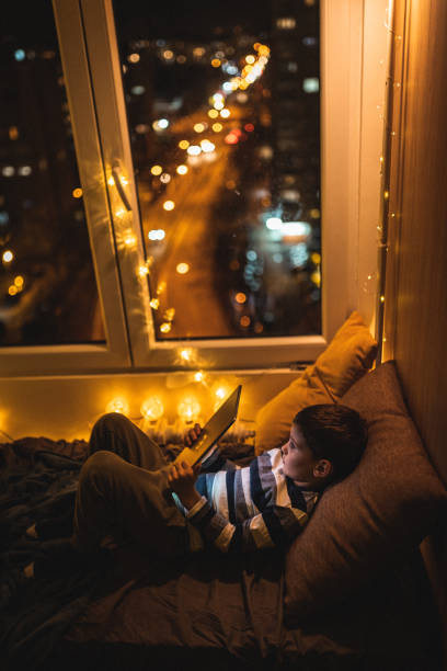 istock Cute little boy lying on bed and reading book on tablet 1250342430