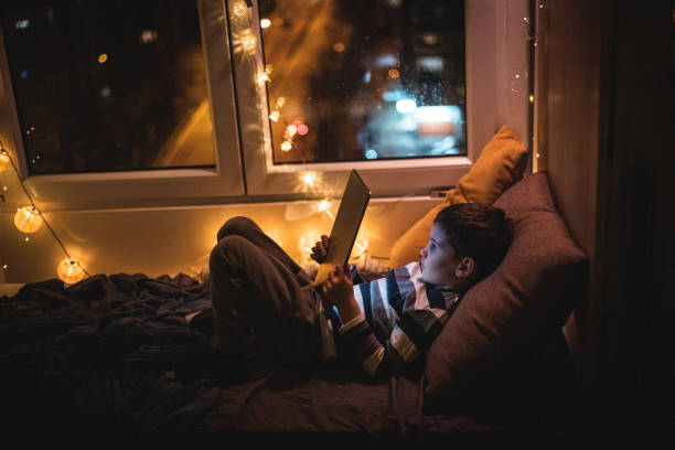 istock Boy lying on bed and reading book on tablet during home isolation 1250343767