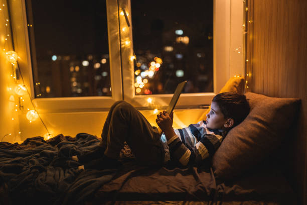 istock Cute little boy lying on bed and reading book on tablet 1250345050