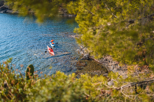 High angle personal perspective of Spanish kayakers paddling close together along shore of Mediterranean Sea off the Costa Brava.