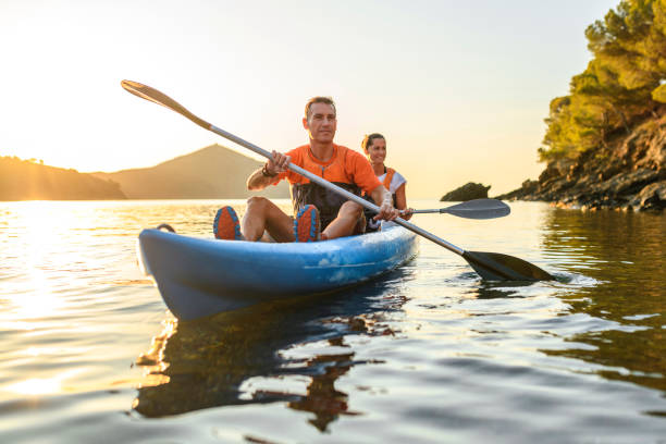 Kayakers Enjoying Healthy Lifestyle in Mediterranean at Dawn Candid portrait of Spanish friends in 30s and 40s pausing to smile at camera while paddling their tandem kayak off the Costa Brava. kayaking photos stock pictures, royalty-free photos & images