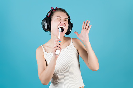 Girl in headphones sings in a toothbrush while brushing teeth on a blue background