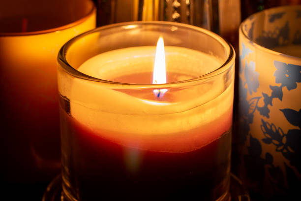 This image shows a close up low light view of a single candle in a glass, warmly illuminating nearby objects.