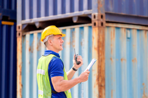 istock Foreman worker in hardhat and safety vest talks on two-way radio control loading containers box from cargo 1250372325