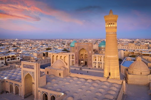 Aerial Sunset Twilight View over the famous Old Town in the City of Bukhara with the iconic Kalyan Minaret - Kalon Minor and Miri Arab Madressa. Aerial Drone Point of View. Itchan Kala, Bukhara, Khorezm Region, Uzbekistan, Central Asia.