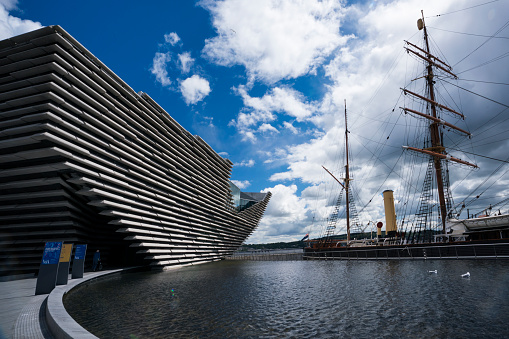 Dundee, Scotland, UK - June 21, 2019: The contemporary V&A designed by architect Kengo Kuma, Scotland's first design museum, which opened in 2018 has 2,466 stone panels arranged into the shape of a ship to acknowledge the ship building heritage of the city. It sits in a harbor next to Shackleton's vintage ship that traveled to Antarctica.