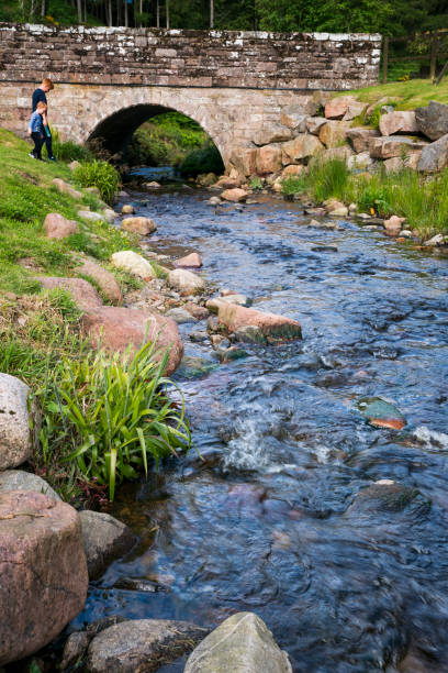 Brechin, Scotland, UK - June 22, 2019: Two young boys walk down to a scenic creek with a curved stone bridge, Brechin, Scotland, UK, Europe