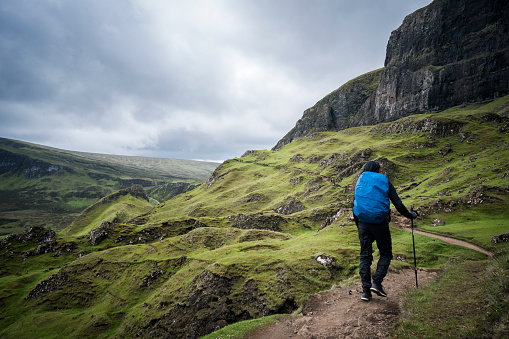 Isle of Skye, Scotland, UK - June 9, 2019: A backpacker uses a hiking pole to walk along the famous Quiraing hiking trail on a cloudy overcast day, Europe