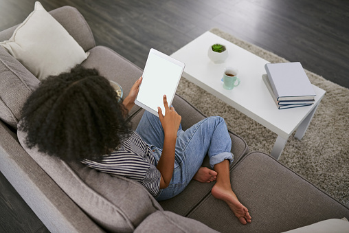 Shot of a young woman using a digital tablet on the sofa at home