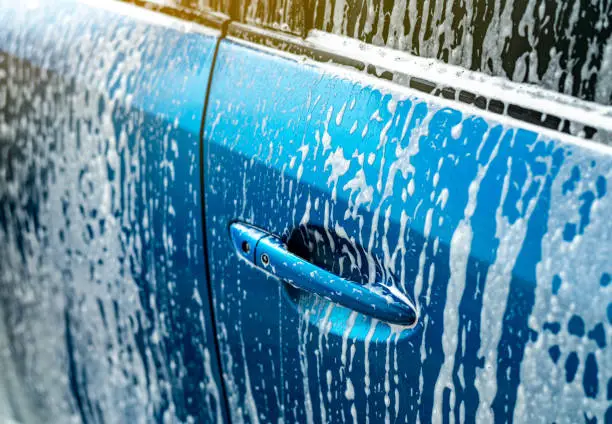 Blue car wash with white soap foam. Auto care business. Car cleaning and shining before waxing service. Vehicle cleaning service with antiseptic and disinfection of coronavirus (COVID-19). Carwash.