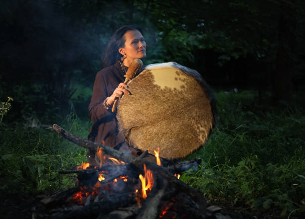 Shamanic woman conducts ritual at night in the forest by the fire