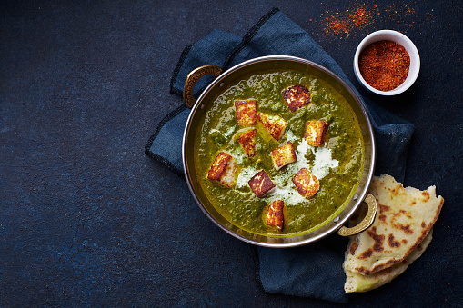 Flat lay top view of vegetarian palak paneer starter. Indian cuisine, curry dish with soft cheese and spinach on concrete background with copy space