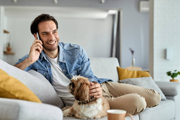istock Happy man talking on mobile phone while relaxing with his dog at home. 1250400839