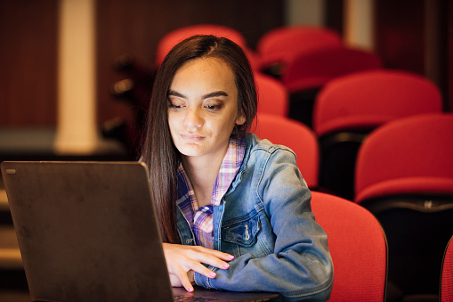 A shot of a young, Polynesian woman using her laptop whilst in a classroom, Perth, Australia. She is living with hearing impairment, cerebral palsy, and epilepsy.