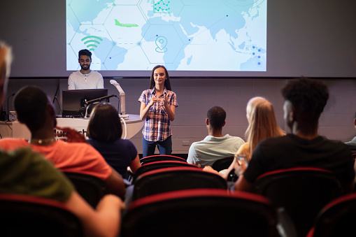 A shot of a group of students taking part in a lecture at a university in Perth, Australia. One of the students is living with hearing impairment is presenting a slideshow using sign language.