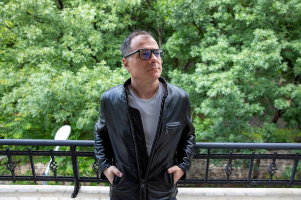 Portrait of middle aged man with eyeglasses wearing weather jacket standing on the balcony of his home